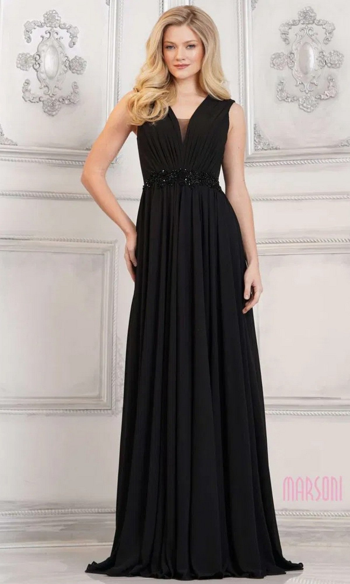 A woman stands in an ornate room wearing the Marsoni MV1292, a sleeveless, floor-length black formal dress with a V-neckline, ruched bodice, and beaded waist detail.